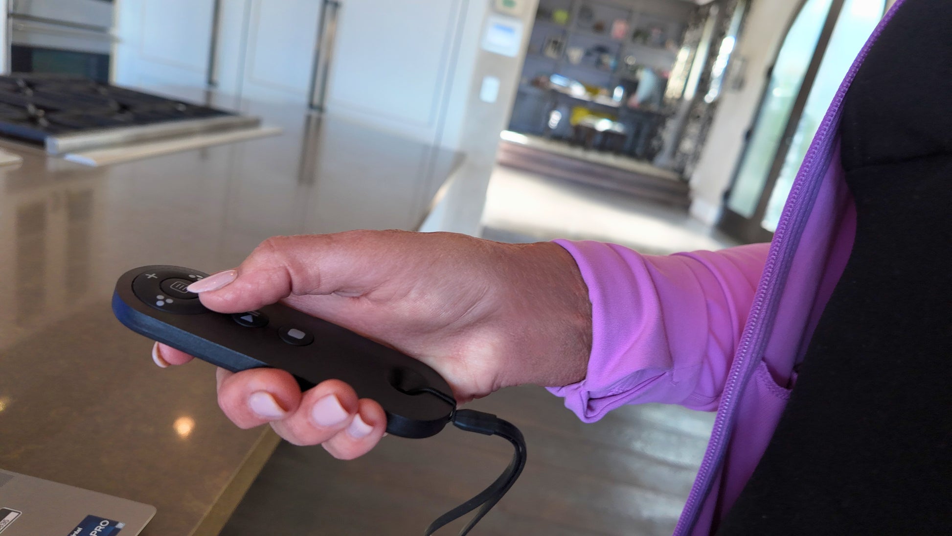 Person holding a black remote control in a room with a desk and computer while walking on a under desk treadmill.