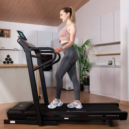 A woman in a pink sports bra and gray leggings walks on a black LifeSmart TM2303 treadmill in a modern kitchen setting.